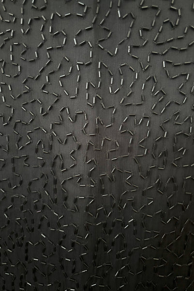 Detail view of 1980s vintage Art Deco faux pearl, silver and black glass beaded black silk chiffon evening dress, size small to medium. With a scoop neckline, sleeveless bodice, and floor length pencil skirt. Showing a close up of the black silk chiffon skirt embellished with black glass bugle beads.