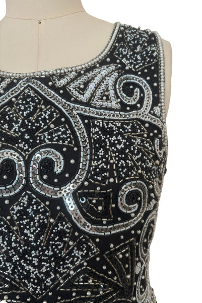 Detail view of 1980s vintage Art Deco faux pearl, silver and black glass beaded black silk chiffon evening dress, size small to medium. With a scoop neckline, sleeveless bodice, and floor length pencil skirt. Showing a close up of the bodice with the silver, white, and black bead and sequin embellished Deco style motif.