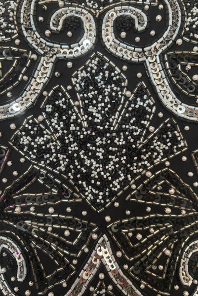 Detail view of 1980s vintage Art Deco faux pearl, silver and black glass beaded black silk chiffon evening dress, size small to medium. With a scoop neckline, sleeveless bodice, and floor length pencil skirt. Showing a close up of the bodice with the silver, white, and black bead and sequin embellished Deco style motif.