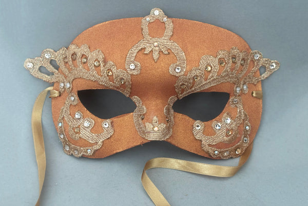 Horizontal detail view of 1990s gold Lurex lace, gold Swarovski crystal, and metallic green painted half mask with gold satin ribbon ties. Showing the light gold and gold Swarovski crystals.