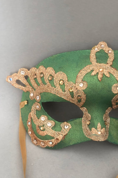 Vertical detail view of 1990s gold Lurex lace, gold Swarovski crystal, and metallic green painted half mask with gold satin ribbon ties. Showing the light gold and gold Swarovski crystals.