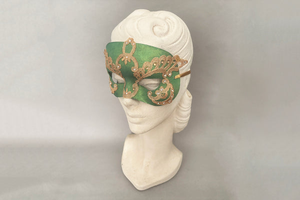 Horizontal 3/4 view of 1990s gold Lurex lace, gold Swarovski crystal, and metallic green painted half mask with gold satin ribbon ties. Showing the mask on a mannequin head.