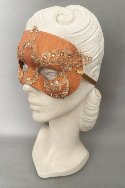 Vertical 3/4 view of 1990s gold Lurex lace, gold Swarovski crystal, and metallic pink rose gold painted half mask with gold satin ribbon ties. Showing the mask on a mannequin head.