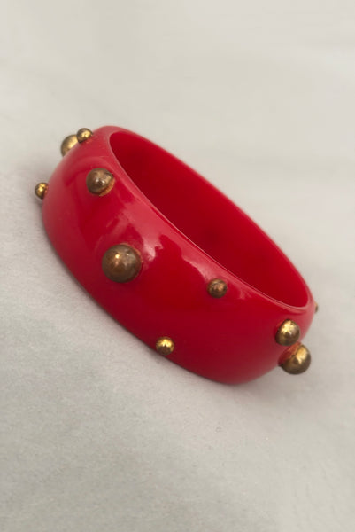 Vertical perspective view of 1940s vintage brass studded rich cherry red Bakelite statement bangle bracelet.