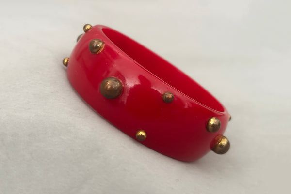 Horizontal perspective view of 1940s vintage brass studded rich cherry red Bakelite statement bangle bracelet.