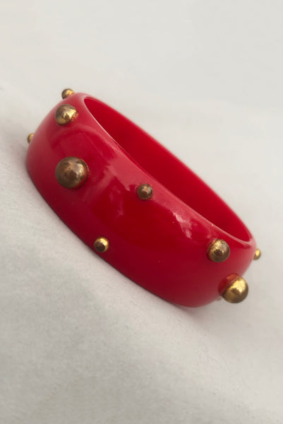 Vertical perspective view of 1940s vintage brass studded rich cherry red Bakelite statement bangle bracelet.