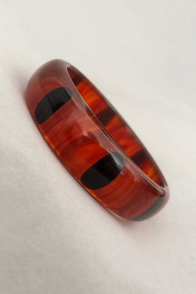 Vertical perspective view of contemporary artisan Christopher Dombek root beer translucent brown Bakelite domed bangle bracelet with inlaid oval black dots.