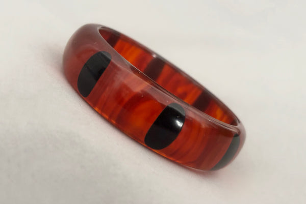Horizontal perspective view of contemporary artisan Christopher Dombek root beer translucent brown Bakelite domed bangle bracelet with inlaid oval black dots.