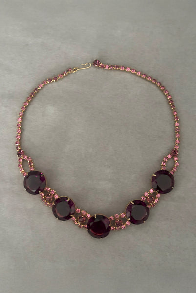 Vertical flat lay front view of 1950s vintage pink and large Purple rhinestone adjustable gold tone necklace.