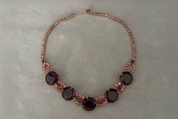 Horizontal flat lay front view of 1950s vintage pink and large Purple rhinestone adjustable gold tone necklace.