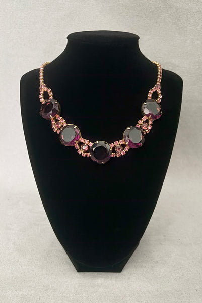 Vertical front view of 1950s vintage pink and large Purple rhinestone adjustable gold tone necklace. Showing the necklace on a display.