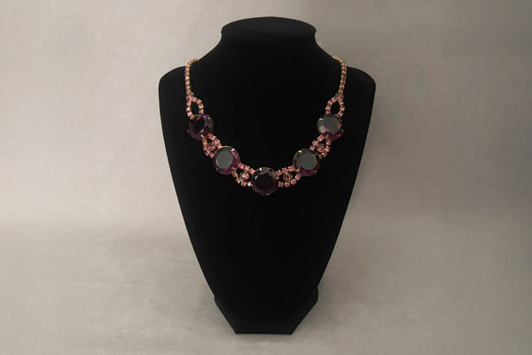 Horizontal front view of 1950s vintage pink and large Purple rhinestone adjustable gold tone necklace. Showing the necklace on a display.