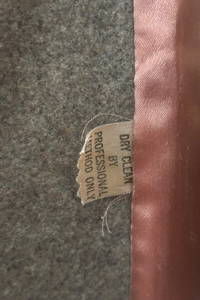 Interior detail view of 1960s vintage heavy gray and rust tie waist wool coat by Carol Cohen for Braefair, size medium to large. Showing the dry clean only tag.