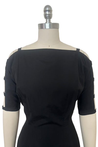 Bodice front view of 1950s vintage black boat neck, raglan open sleeve wiggle dress, size small to medium. Showing the boat neckline and open top sleeves.