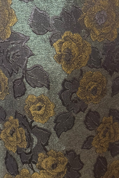 Detail view of 1950s vintage black velvet crew neck, sleeveless, green floral brocade pencil skirt cocktail dress, with beaded belt, size medium to large. Showing a close up of the dark green floral brocade with chartreuse and black roses.