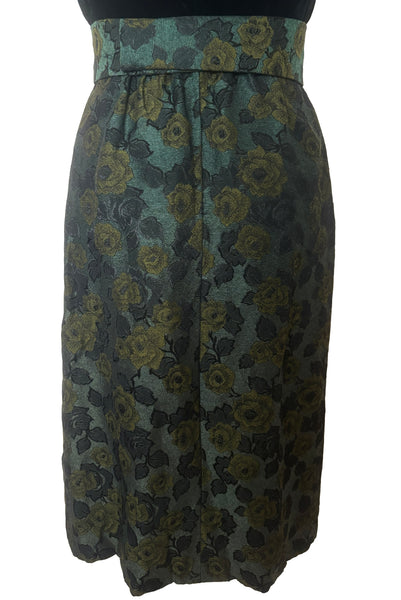 Skirt back view of 1950s vintage black velvet crew neck, sleeveless, green floral brocade pencil skirt cocktail dress, with beaded belt, size medium to large. Showing the belt wrapping around the back and closing with hooks.