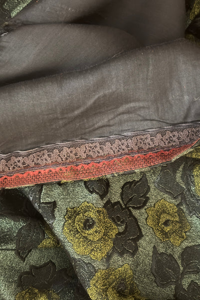 Detail view of 1950s vintage black velvet crew neck, sleeveless, green floral brocade pencil skirt cocktail dress, with beaded belt, size medium to large. Showing the black voile underlining and lace faced hem.