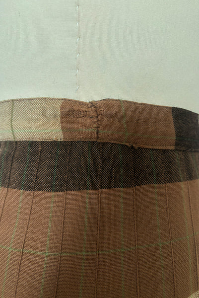 Detail view of 1970s vintage reversible black, tan, cream, and green wool plaid pleated midi skirt by Charlotte Ford for Classique Collection, size medium to large. Showing the repaired waistband seam on the lighter side.