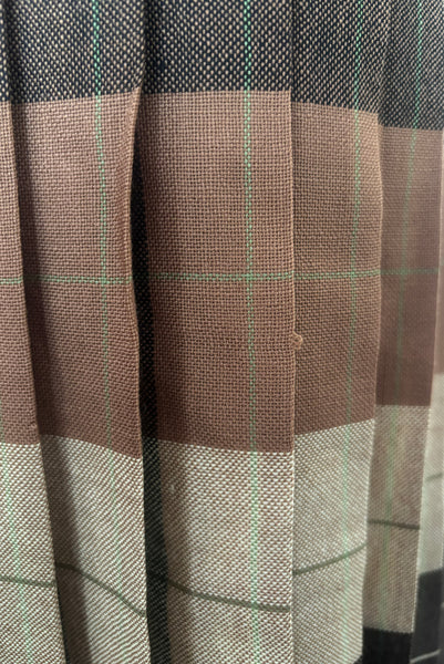 Detail view of 1970s vintage reversible black, tan, cream, and green wool plaid pleated midi skirt by Charlotte Ford for Classique Collection, size medium to large. Showing a pulled thread on the lighter side.