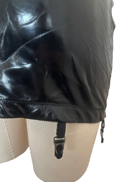 Detail view of 2000s vintage goth pin-up black wet look nylon Lycra stretch lingerie garter skirt by Bernie Dexter, size medium to large. Showing a close-up of the elastic at the bottom edge and the garter clip.