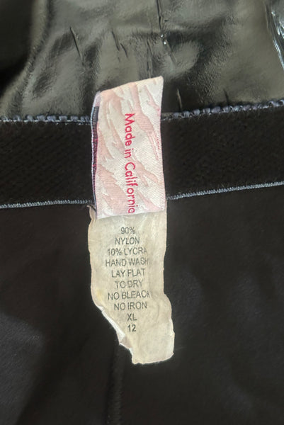 Interior detail view of 2000s vintage goth pin-up black wet look nylon Lycra stretch lingerie garter skirt by Bernie Dexter, size medium to large. Showing a close-up of the fabric content and size XL/12 tag.
