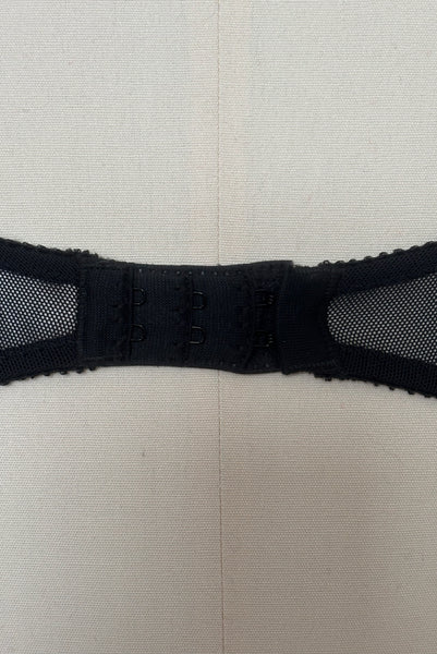 Detail view of 2000s vintage y2k goth pin-up lingerie black nylon Lycra wet look bra by Bernie Dexter for Lucy B, size medium to large. Showing a close-up of the black mesh back and hook & eye closure.