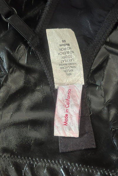 Interior detail view of 2000s vintage y2k goth pin-up lingerie black nylon Lycra wet look bra by Bernie Dexter for Lucy B, size medium to large. Showing a close-up of the fabric composition and size M-6/8 tag.