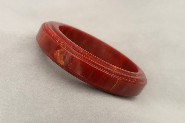 Horizontal perspective view of 1940s vintage groove carved rust and yellow marbled Bakelite bangle bracelet.