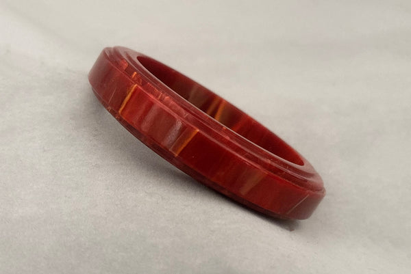 Horizontal perspective view of 1940s vintage groove carved rust and yellow marbled Bakelite bangle bracelet.