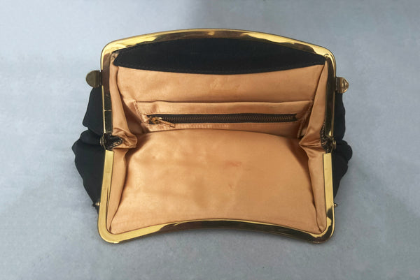 Horizontal interior view of 1950s vintage black faille gold tone metal frame side clasps clutch handbag. Showing the peach satin lining.