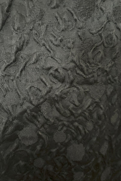 Fabric detail view of 1960s vintage black matelassé jacquard Mod cocktail dress and red satin lined wrap, size medium to large.