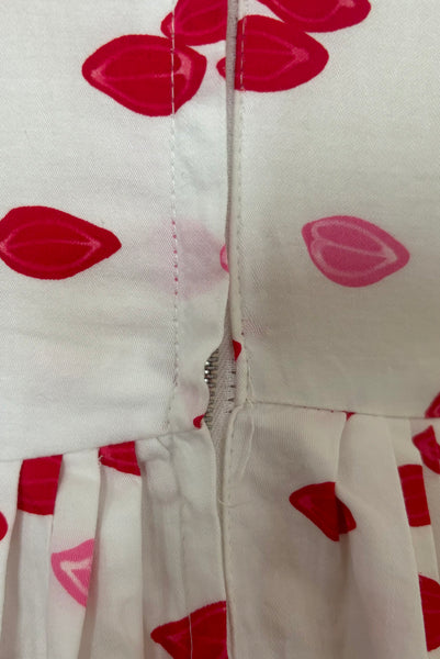 Detail of 1950s vintage red and pink lips novelty border print white cotton sleeveless, full gathered skirt dress, size extra small to small. Showing stress at the zipper seam.