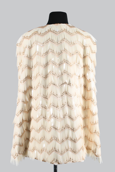 The Leslie Courreges Eleanor Cape features gold sequins against blush embroidery with ivory fringe sequins. 